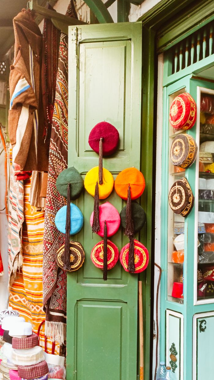 Home A lively market scene showcasing a variety of colorful traditional hats and textiles.