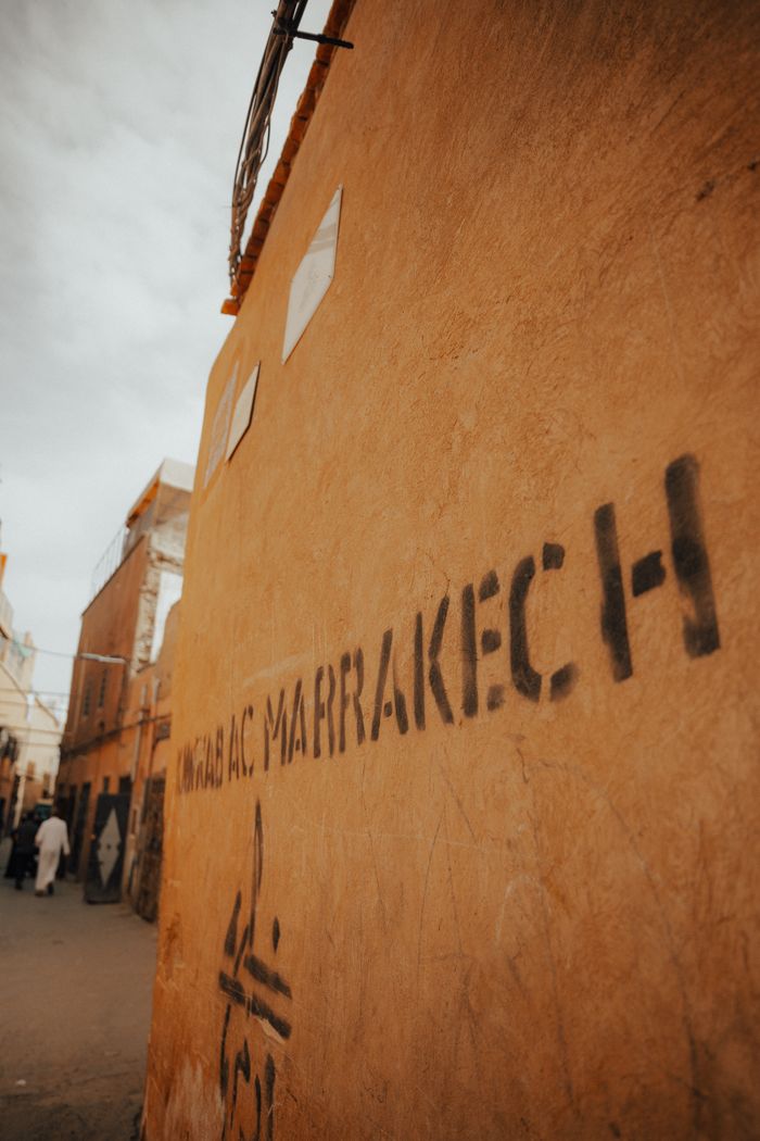 Home Street scene in Marrakech featuring orange-walled graffiti in a narrow urban alleyway.