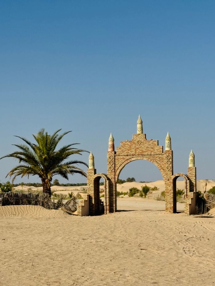 Home A solitary brick archway in a desert landscape with clear blue skies above.